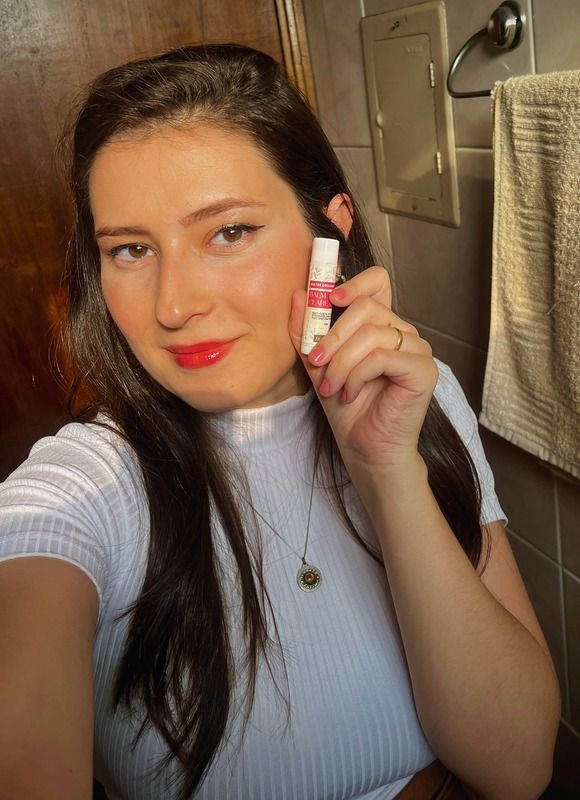 Gabi apresenta um produto de cuidado labial diante do espelho.