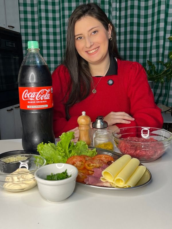 Gabi na cozinha com Coca-Cola e ingredientes para preparar hambúrguer.