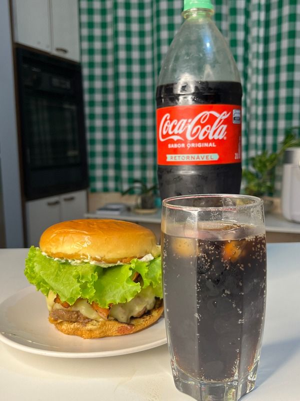 Hambúrguer artesanal acompanhado de um copo e uma garrafa de Coca-Cola.