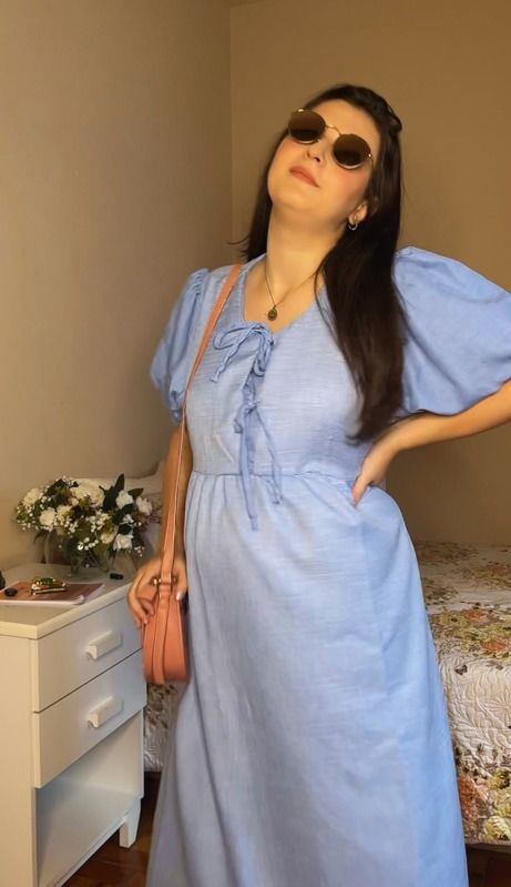 Gabi posa de óculos escuros com um vestido azul e bolsa a tiracolo.